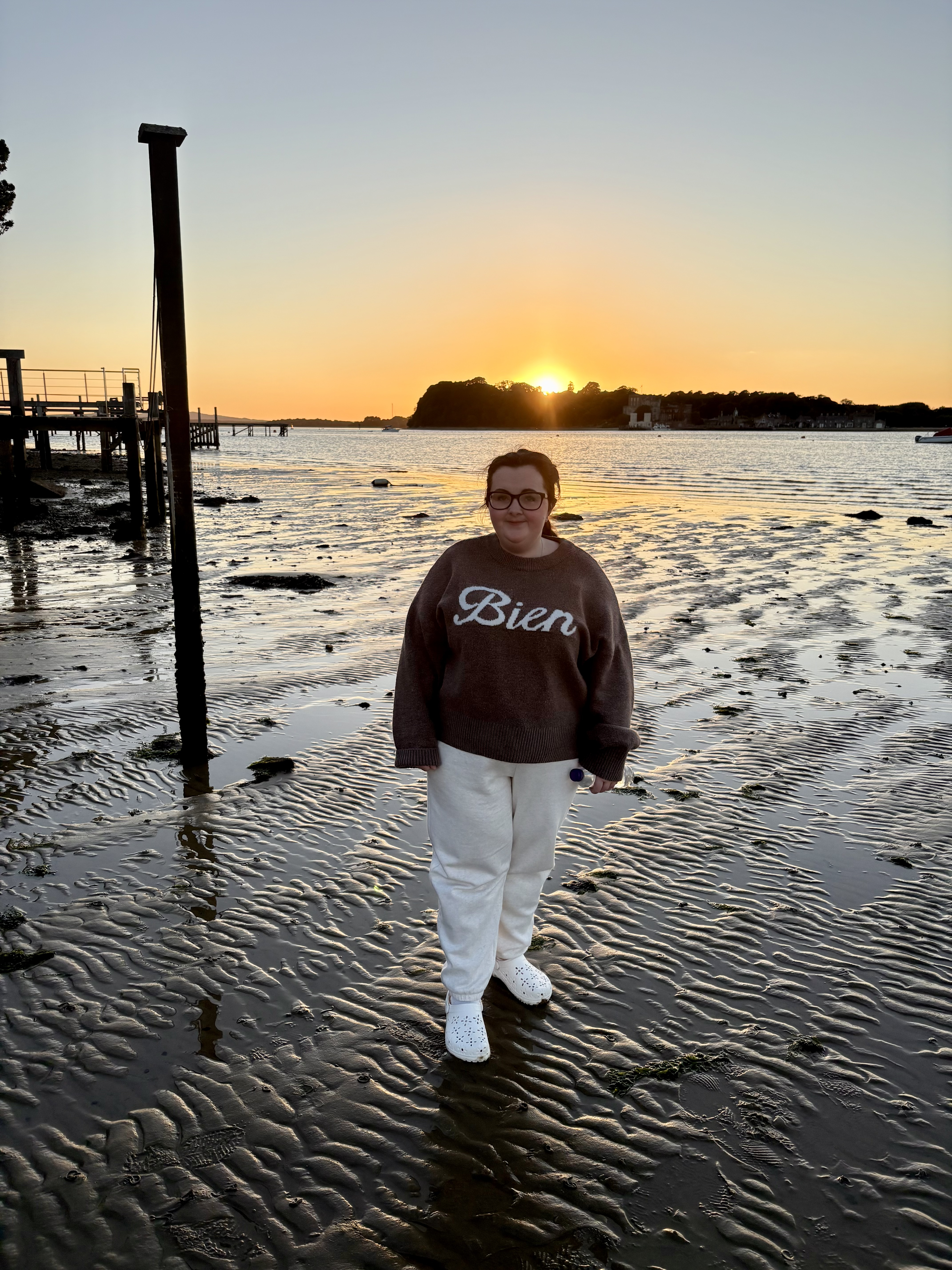 Tasmin, a young women with MCAS stood on a beach with the tide out at sunset