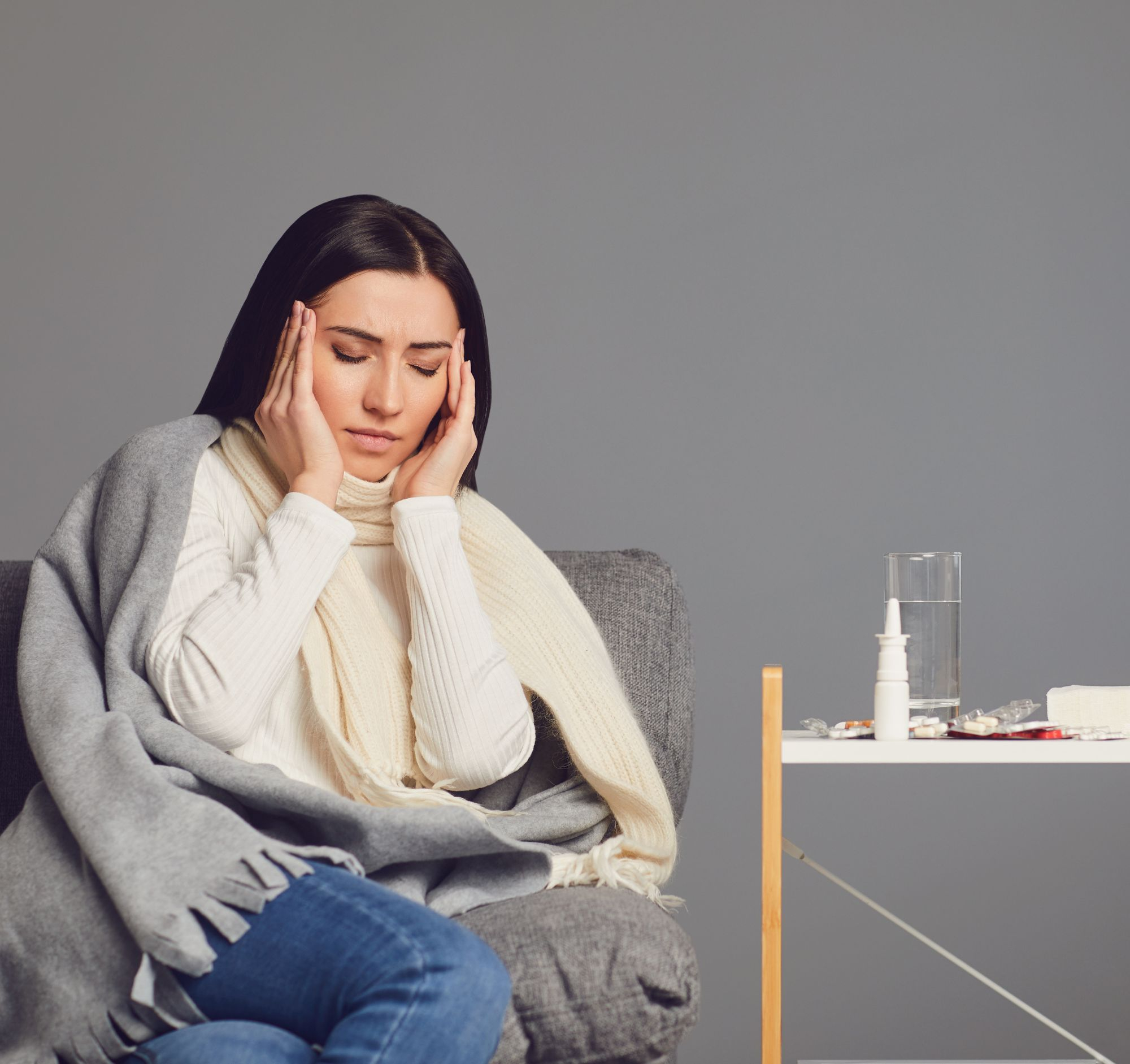 A lady sat in a chair with a blanket around shoulders , eyes closed and hands on her temples