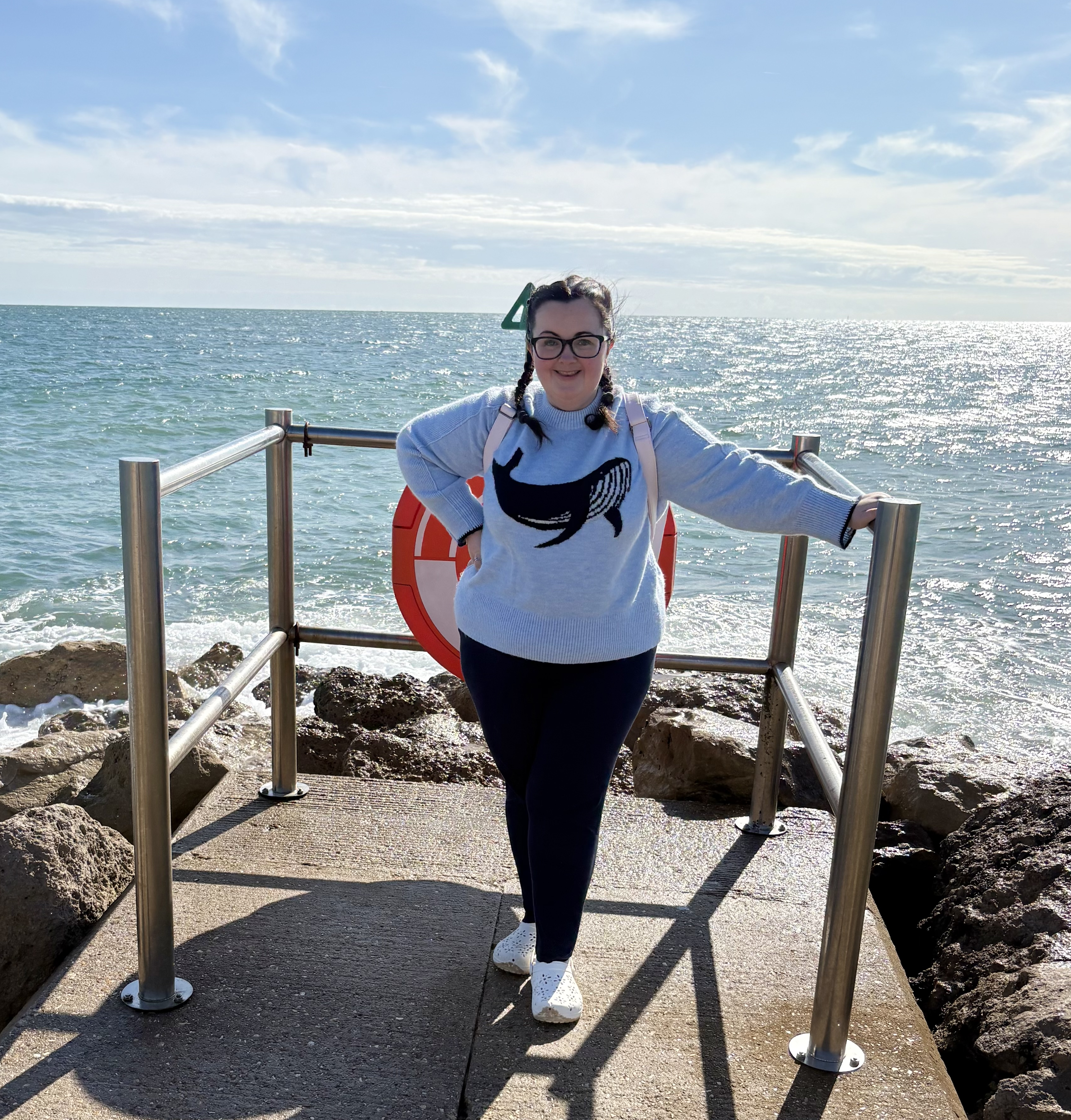 Tamsin, a young women with MCAS stood on a pier with the sea in the background